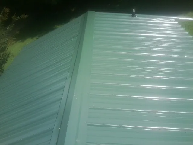 New green metal panels meeting at the ridge of a roof — Flat Roof Repair work by our crew in Melville