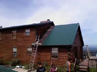 Green metal roof going on a two story log home with ladders set in Melville